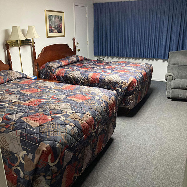 A clean hotel room with two queen beds, a recliner and closed curtains