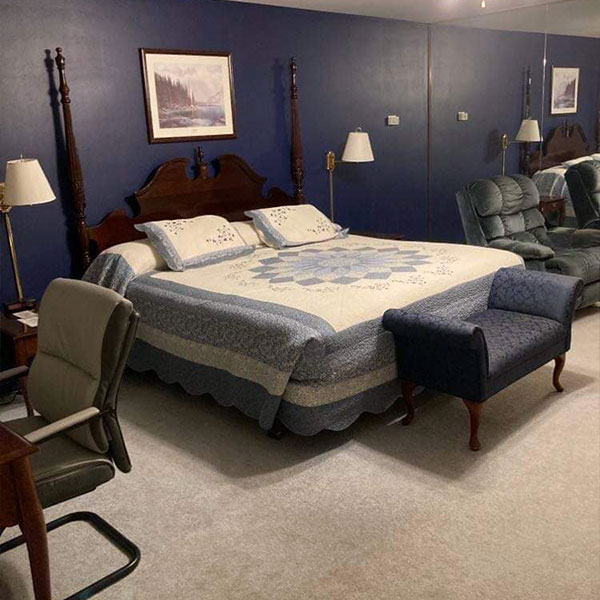 A blue themed suite with a desk, recliner and made bed with comforter