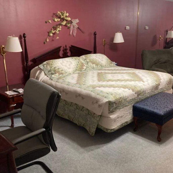 A red themed suite with a desk, recliner and made bed with comforter