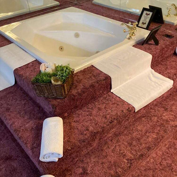 A jacuizi bathtub on a platform with rolled towles and toiletries